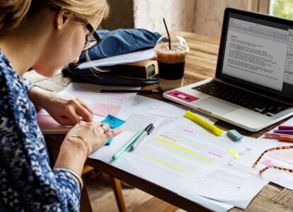 A student highlighting notes and working on assignments with a laptop and study materials, preparing for business courses at Peterborough College, UK, in a productive learning environment.